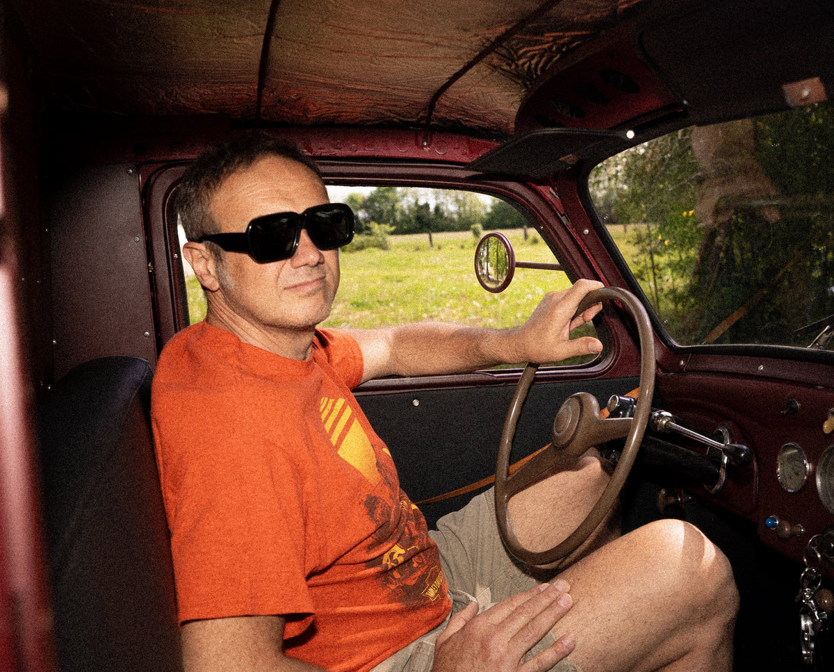 Uomo con occhiali da sole alla guida di un'auto d'epoca, immagine della collezione RobyMarton Gin